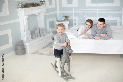 Happy family of three sit in room and play with daughter on her wooden toy horse