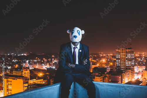 Tablou pe pânză Man wearing a mask sitting on the ledge of a building