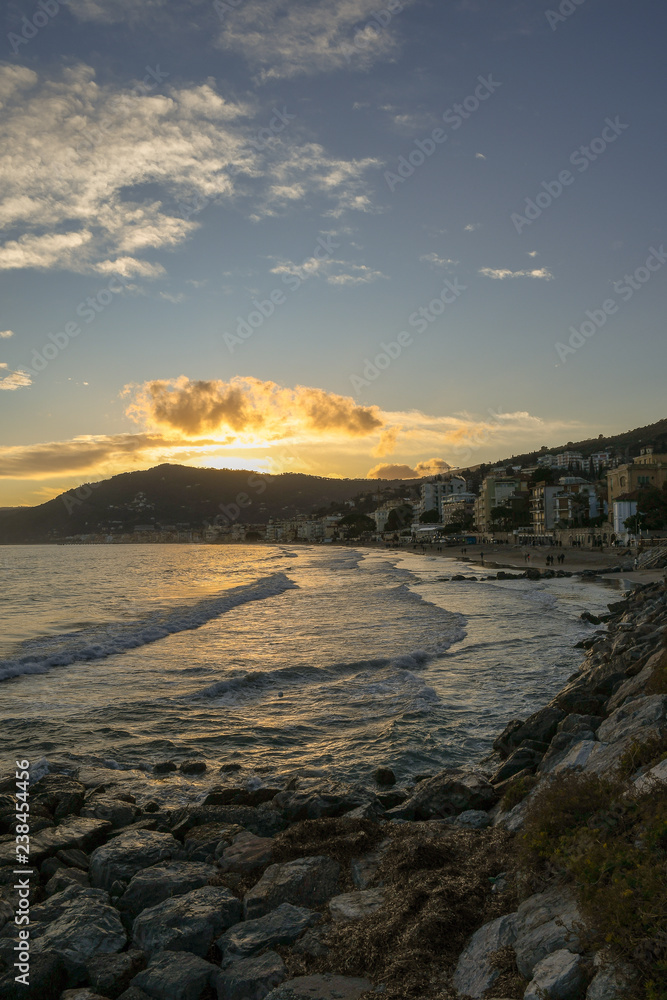 View from a rocky beach of a coastal city at sunset in winter, Alassio, Liguria, Italy