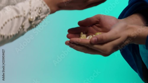 Close up for eastern young woman hands giving many small seashells to man hands, barter concept. Stock. Eastern woman in white dress holding and passing many small seashels to a man. photo