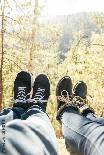 two pairs of legs in boots against a background of trees