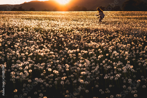 Young woman in yellow spring dandelion field in warm sunset light. Romantic photo on the meadow