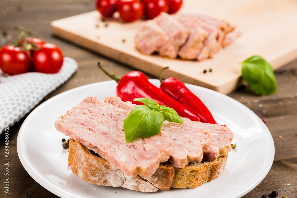 Slice of bread with preserved ham and peppers. White plate on a wooden background
