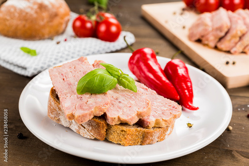 Slice of bread with preserved ham and peppers. White plate on a wooden background