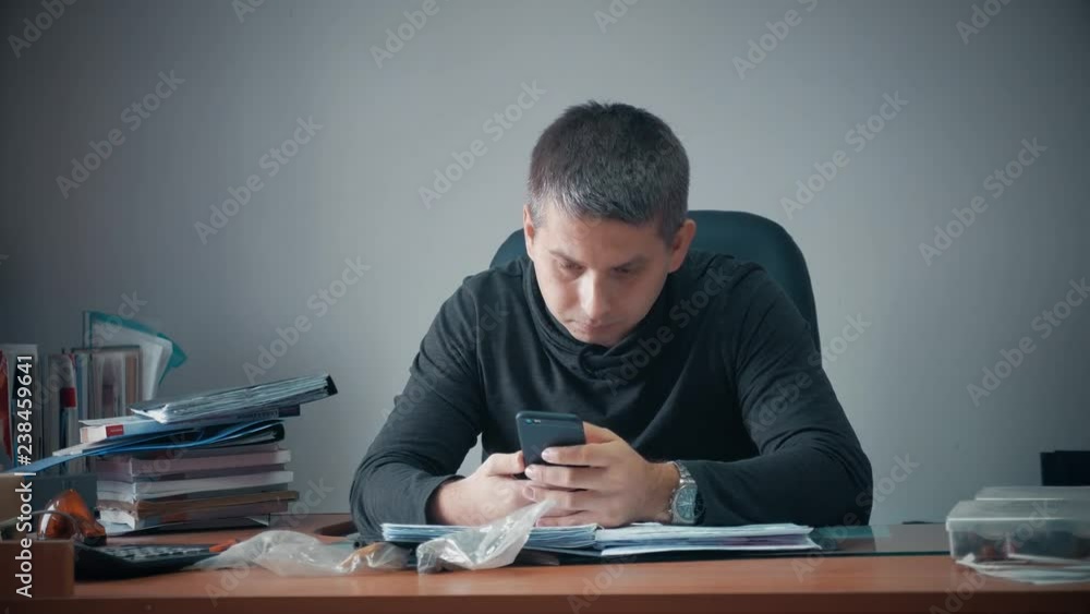 Happy young businessman sitting in office with business papers on table. Handsome man working, writing at desk in home office. Home office work concept. Happy young businessman sitting in office with business papers on table. Handsome man working, writing at desk in home office. Home office work concept.