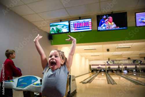 Excited sister screaming while brother holding ball at bowling alley