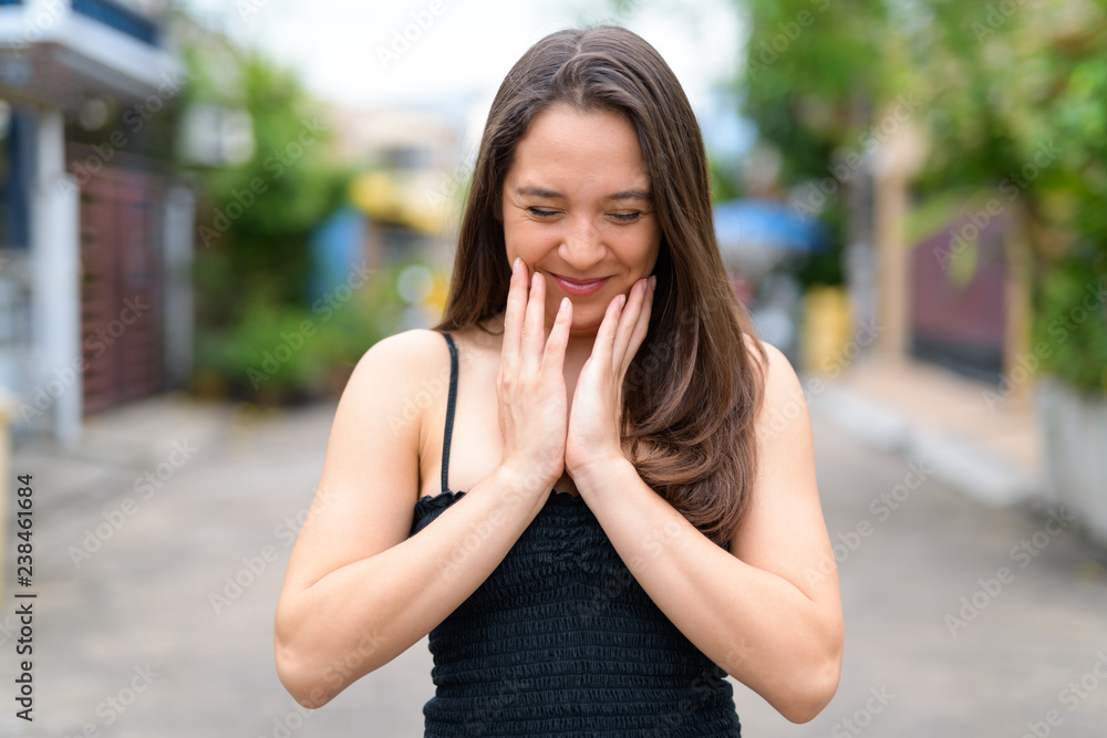 Young happy multi-ethnic woman smiling and touching face outdoors Young happy multi-ethnic woman smiling and touching face outdoors