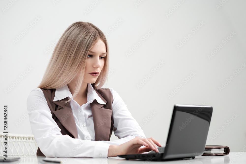 Blonde girl in a business suit works on a computer in a white bright office. Blonde girl in a business suit works on a computer in a white bright office.