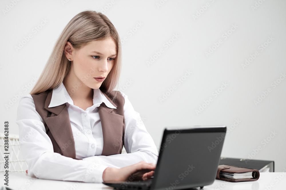 Blonde girl in a business suit works on a computer in a white bright office. Blonde girl in a business suit works on a computer in a white bright office.