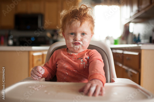 Boy with messy face puckering lips on high chair at home photo