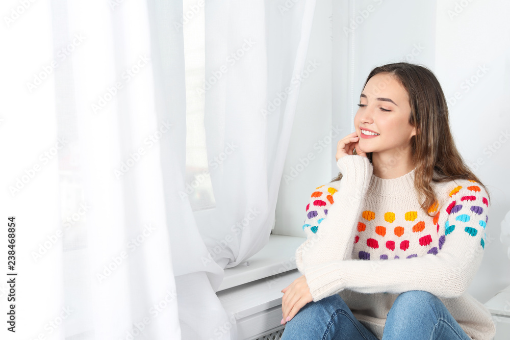 Beautiful teenage girl in warm cozy sweater looking out window at home. Space for text Beautiful teenage girl in warm cozy sweater looking out window at home. Space for text