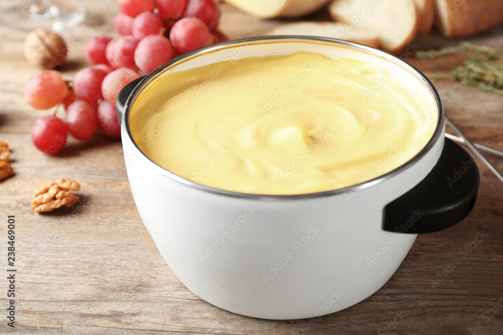 Pot with delicious cheese fondue on wooden table Pot with delicious cheese fondue on wooden table
