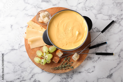 Flat lay composition with pot of delicious cheese fondue on marble table