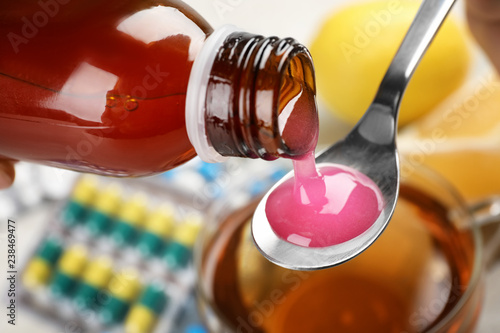 Pouring cough syrup from bottle into spoon on blurred background, closeup