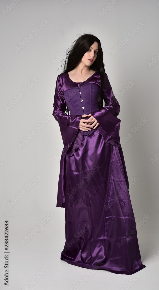 full length portrait of beautiful girl with long black hair, wearing purple fantasy medieval gown. standing pose on grey studio background. full length portrait of beautiful girl with long black hair, wearing purple fantasy medieval gown. standing pose on grey studio background.