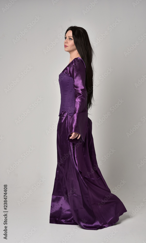 full length portrait of beautiful girl with long black hair, wearing purple fantasy medieval gown. standing pose on grey studio background. full length portrait of beautiful girl with long black hair, wearing purple fantasy medieval gown. standing pose on grey studio background.