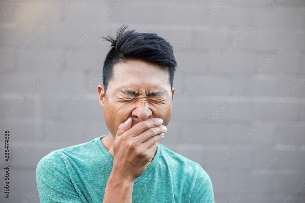 Close-up of man with hands covering mouth while yawning against wall Close-up of man with hands covering mouth while yawning against wall