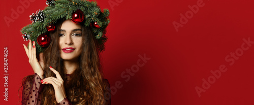 Beautiful woman with Christmas spruce fir wreath with cones and new year decoration balls on red 