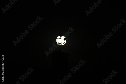 Tableau sur toile Moon rises against the silhouette of a weather vane