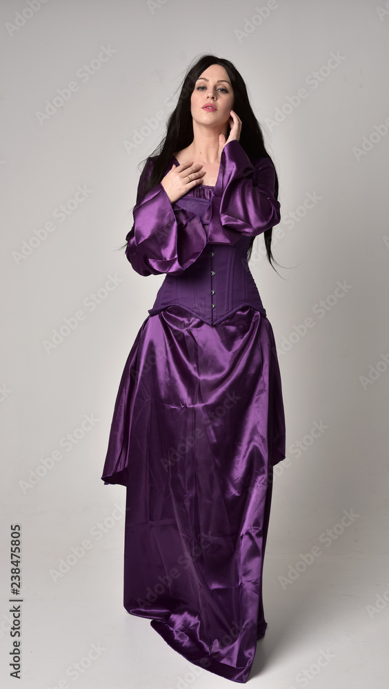 full length portrait of beautiful girl with long black hair, wearing purple fantasy medieval gown. standing pose on grey studio background. full length portrait of beautiful girl with long black hair, wearing purple fantasy medieval gown. standing pose on grey studio background.