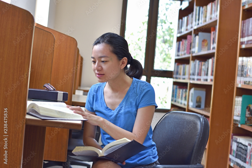 Asian woman doing research and reading book in public library. Asian woman doing research and reading book in public library.