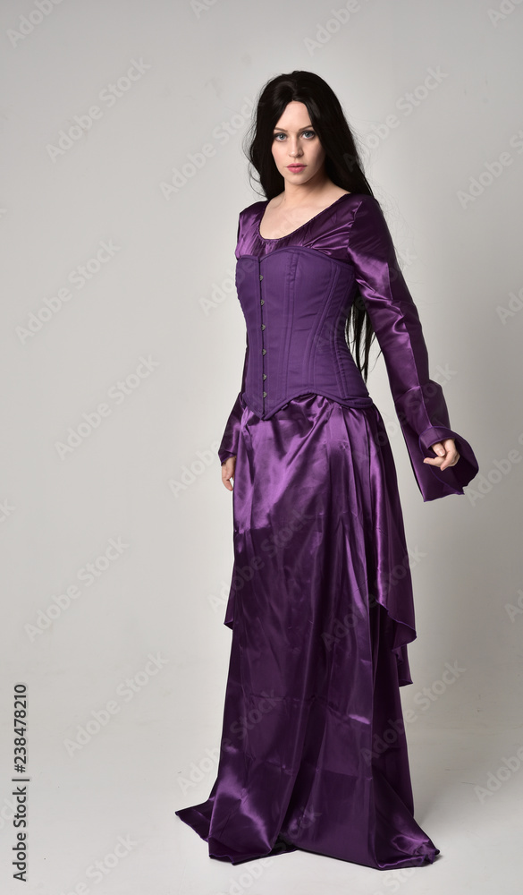 full length portrait of beautiful girl with long black hair, wearing purple fantasy medieval gown. standing pose on grey studio background. full length portrait of beautiful girl with long black hair, wearing purple fantasy medieval gown. standing pose on grey studio background.
