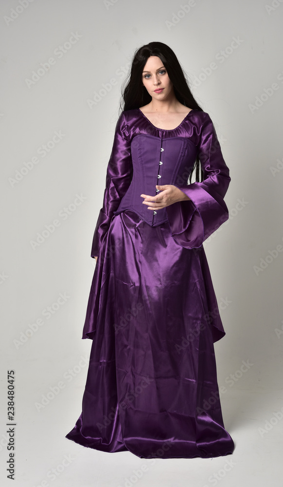 Fototapeta premium full length portrait of beautiful girl with long black hair, wearing purple fantasy medieval gown. standing pose on grey studio background.