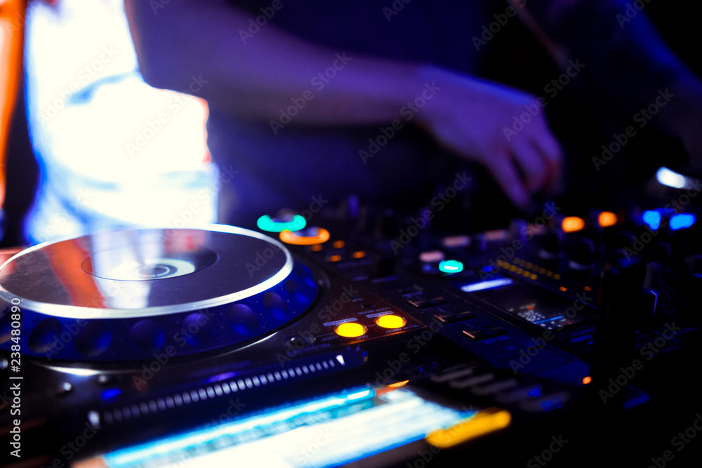 Naklejka premium Disc Jockey mixing deck and turntables at night with colourful illuminated controls for mixing music for a party or disco