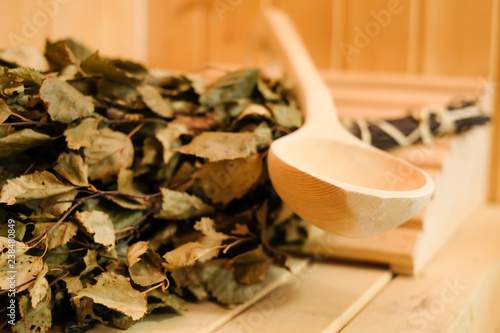 Sauna accessories close up in traditional finnish or russian sauna, birch broom and wooden scoop. Rest and relaxation in the spa to keep warm in the cold winter