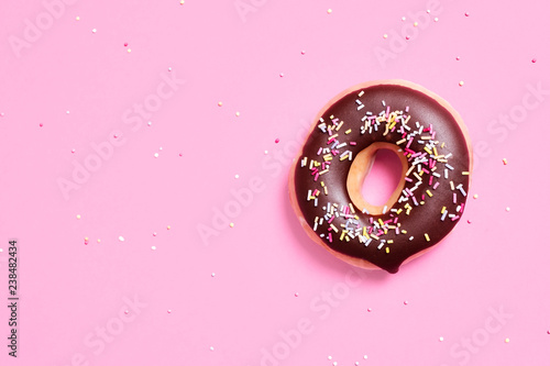 Overhead view of chocolate donut with sprinkles on pink background
