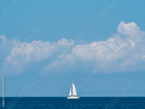 White sailing boat on the horizon with clouds in the background