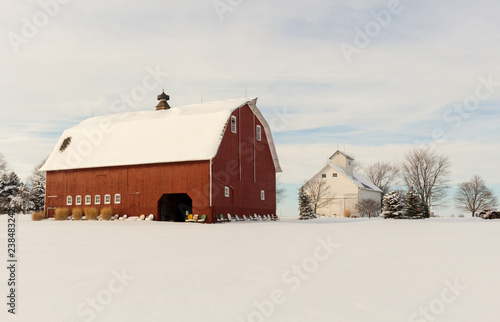 Fototapeta Beautiful winter farm scene with a bright red barn and white corn crib in a snowy field