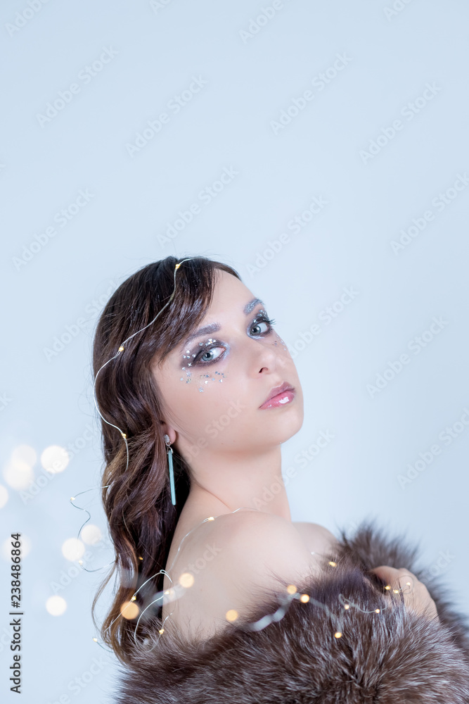 close-up portrait of beautiful curly woman with perfect art make-up, trendy frosted face,eyes design with glitter stones,beads,make up decor. Christmas garland lights.Eco fur coat.expressive eyes.Copy close-up portrait of beautiful curly woman with perfect art make-up, trendy frosted face,eyes design with glitter stones,beads,make up decor. Christmas garland lights.Eco fur coat.expressive eyes.Copy