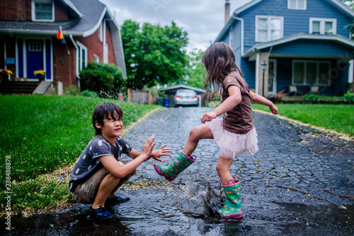 Side view of playful sister splashing puddle on brother during rainy season