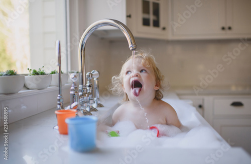 Shirtless girl drinking water from faucet in sink at home photo