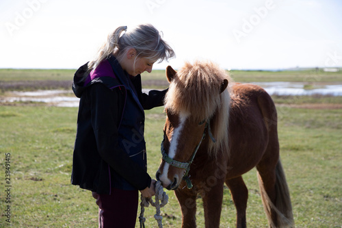 Side view of woman holding knotted rope while standing by horse on field during sunny day photo