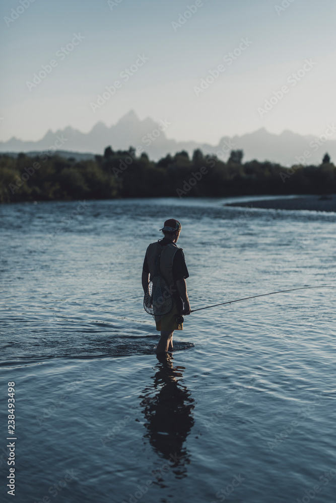 Rear view of man fishing in lake against clear sky during sunset Rear view of man fishing in lake against clear sky during sunset