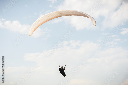 Professional paraglider in a cocoon suit flies high above the ground against the sky