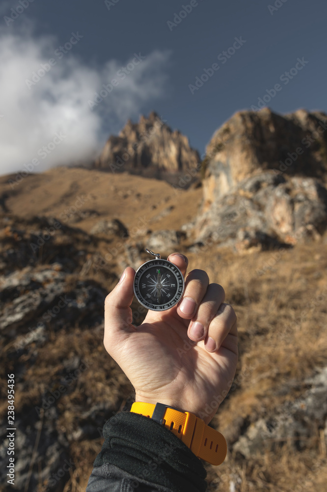 A male Hiker is looking for a direction with a magnetic compass in the mountains in the fall. Point of view shot. Man's hand with a watch bracelet holds a compass A male Hiker is looking for a direction with a magnetic compass in the mountains in the fall. Point of view shot. Man's hand with a watch bracelet holds a compass