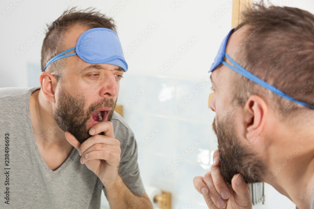 Fototapeta premium Sleepy man looking at mirror and yawning