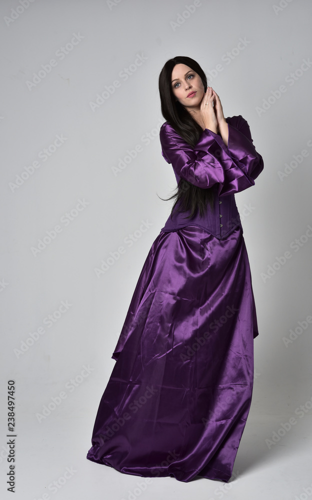 Fototapeta premium full length portrait of beautiful girl with long black hair, wearing purple fantasy medieval gown. standing pose on grey studio background.