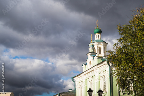 The roof of the church with white turrets and domes with crosses is located on the background of a blue sky with grey clouds