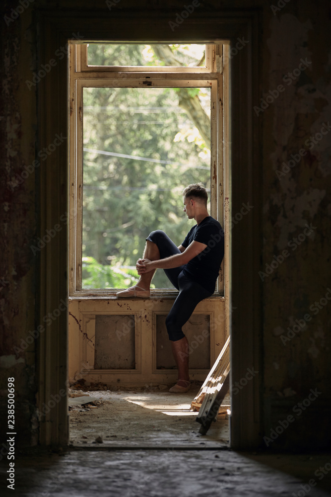Side view of thoughtful male ballet dancer looking through window in old building Side view of thoughtful male ballet dancer looking through window in old building