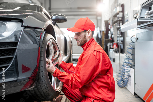 Car service worker in red uniform changing wheel of a sport car at the tire mounting service