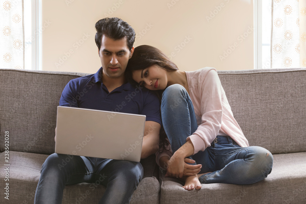 Young couple sitting on sofa using laptop at home	