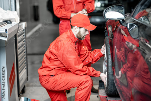 Two car service workers in red uniform changing wheel of a sport car at the tire mounting service