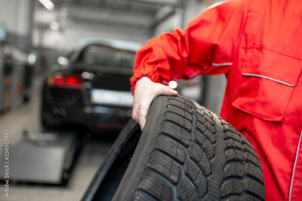 Worker in uniform carrying new tires at the car service or store, close-up view Worker in uniform carrying new tires at the car service or store, close-up view