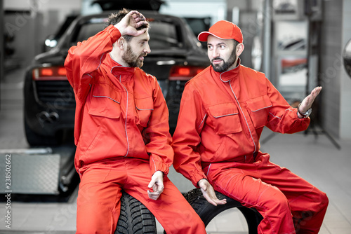Car service workers in red uniform having a break sitting together on the wheels at the tire mounting service
