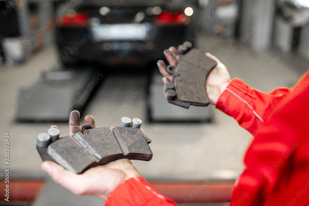Auto mechanic holding new and used brake pads at the car service, close-up view Auto mechanic holding new and used brake pads at the car service, close-up view