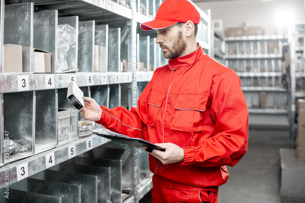 Warehouse worker in red uniform filling some documents checking goods at the storage Warehouse worker in red uniform filling some documents checking goods at the storage